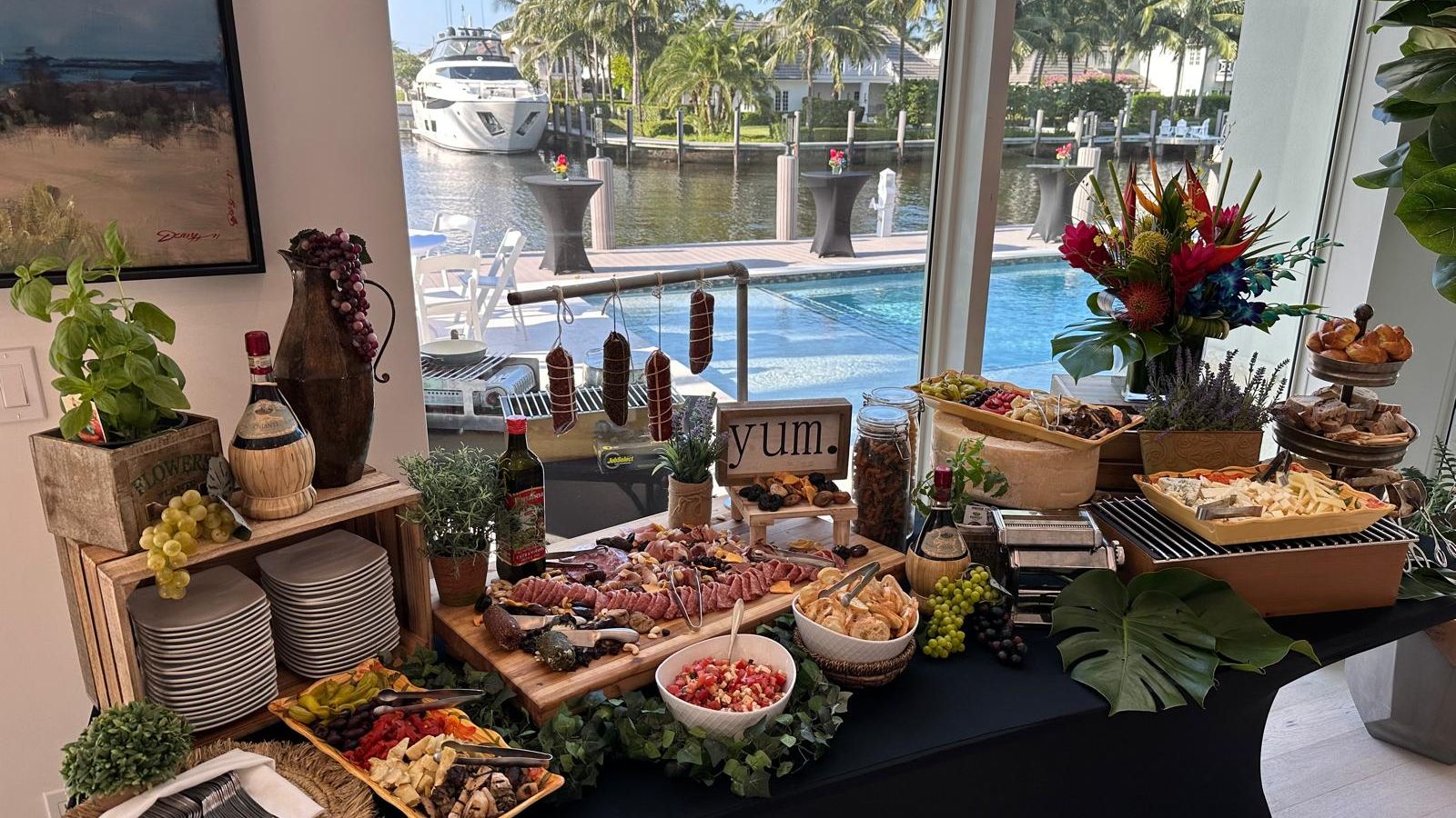 A grazing table set in a waterfront home overlooking a pool, dock and palms