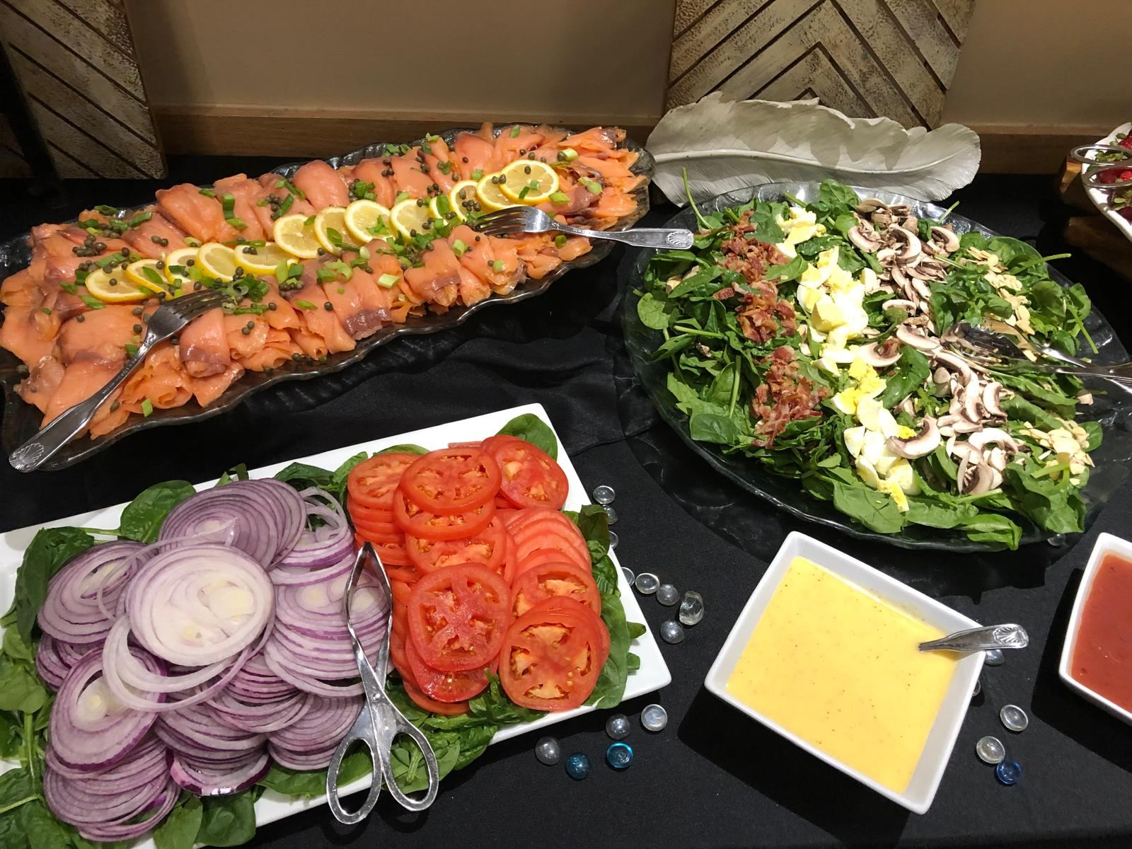 Smoked salmon platter with lemon and capers beside spinach salad